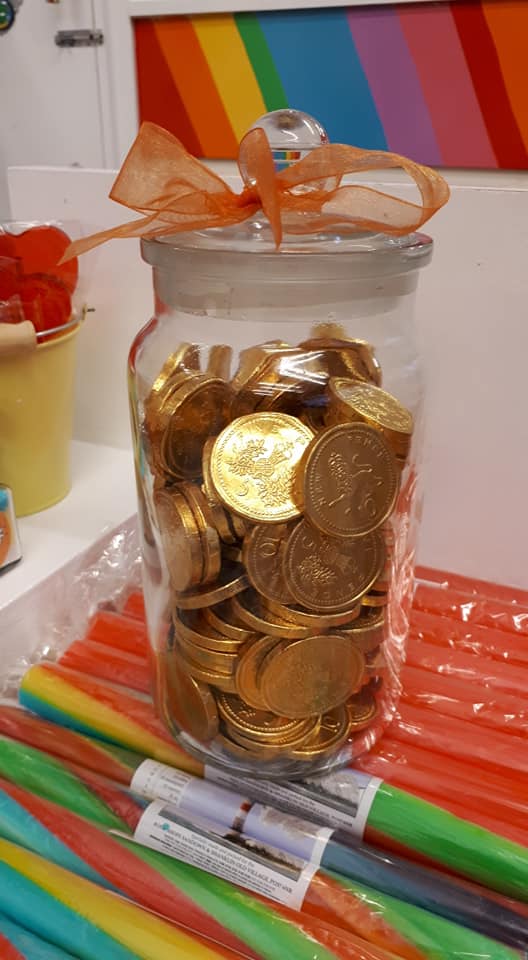 Glass jar filled with gold coins, orange bow, colorful candy sticks.