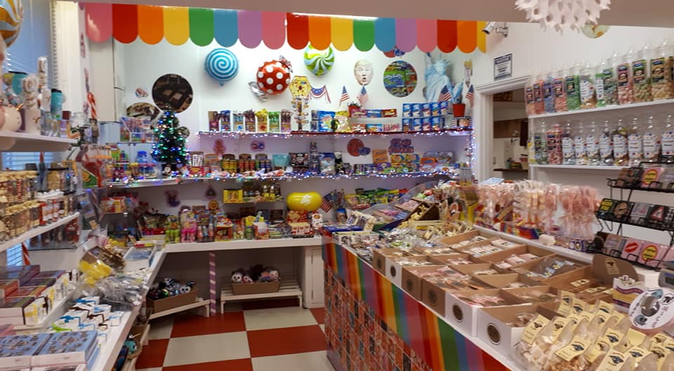 Candy store interior with colorful shelves of sweets, red and white checkered floor, and rainbow decor.