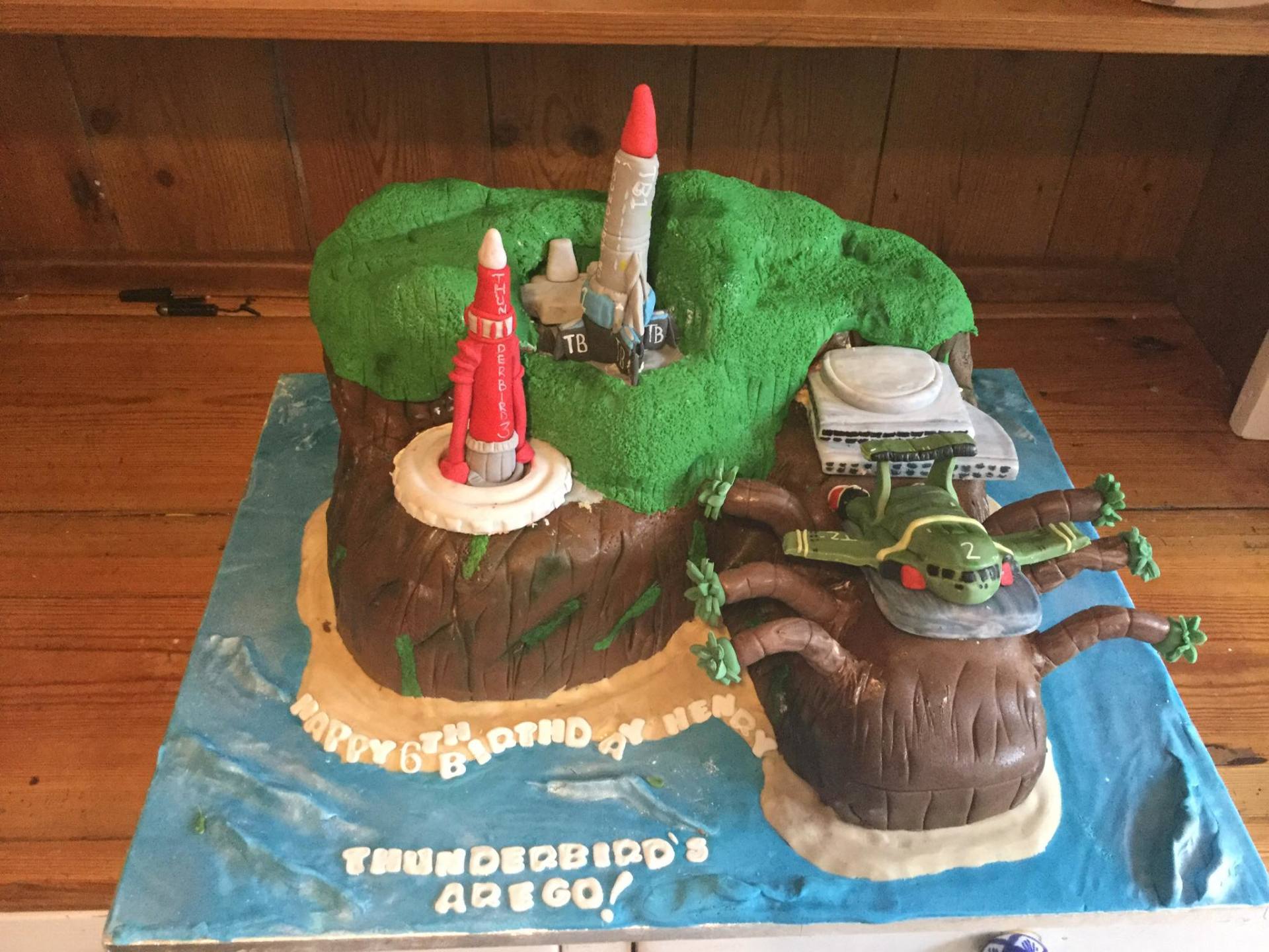 Cake decorated as a Thunderbirds island scene, with a rocket launching, a plane, and the words 