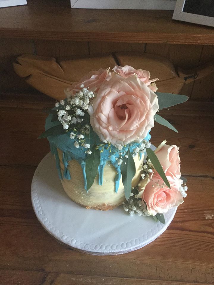 Cake with light blue icing drip, decorated with pink roses and white baby's breath.