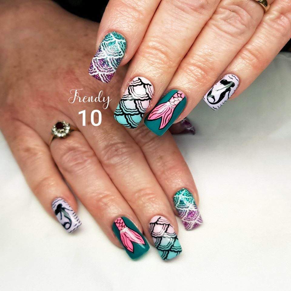 Hands with mermaid-themed nail art. Colors include turquoise, pink, white, and purple. Designs feature scales and silhouettes.