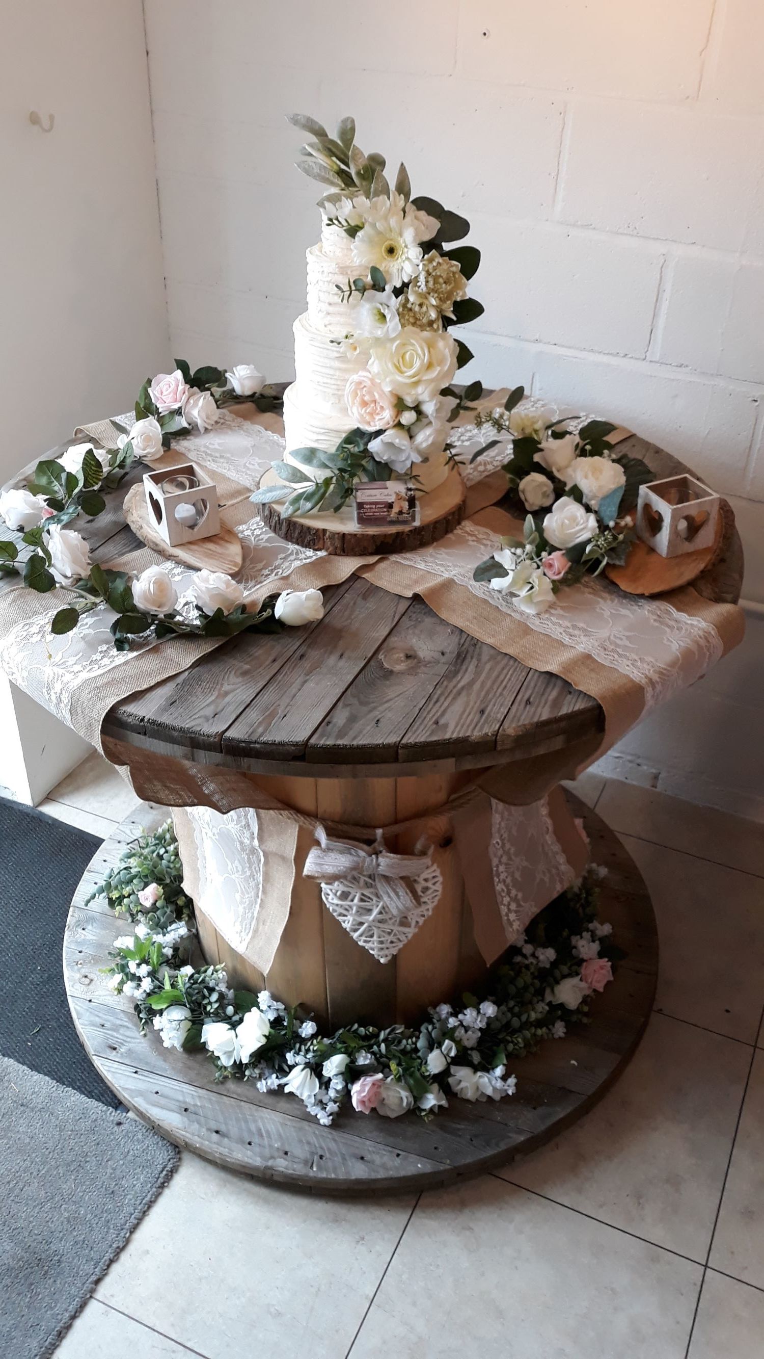 Cake display on a rustic wooden table, decorated with flowers and lace.