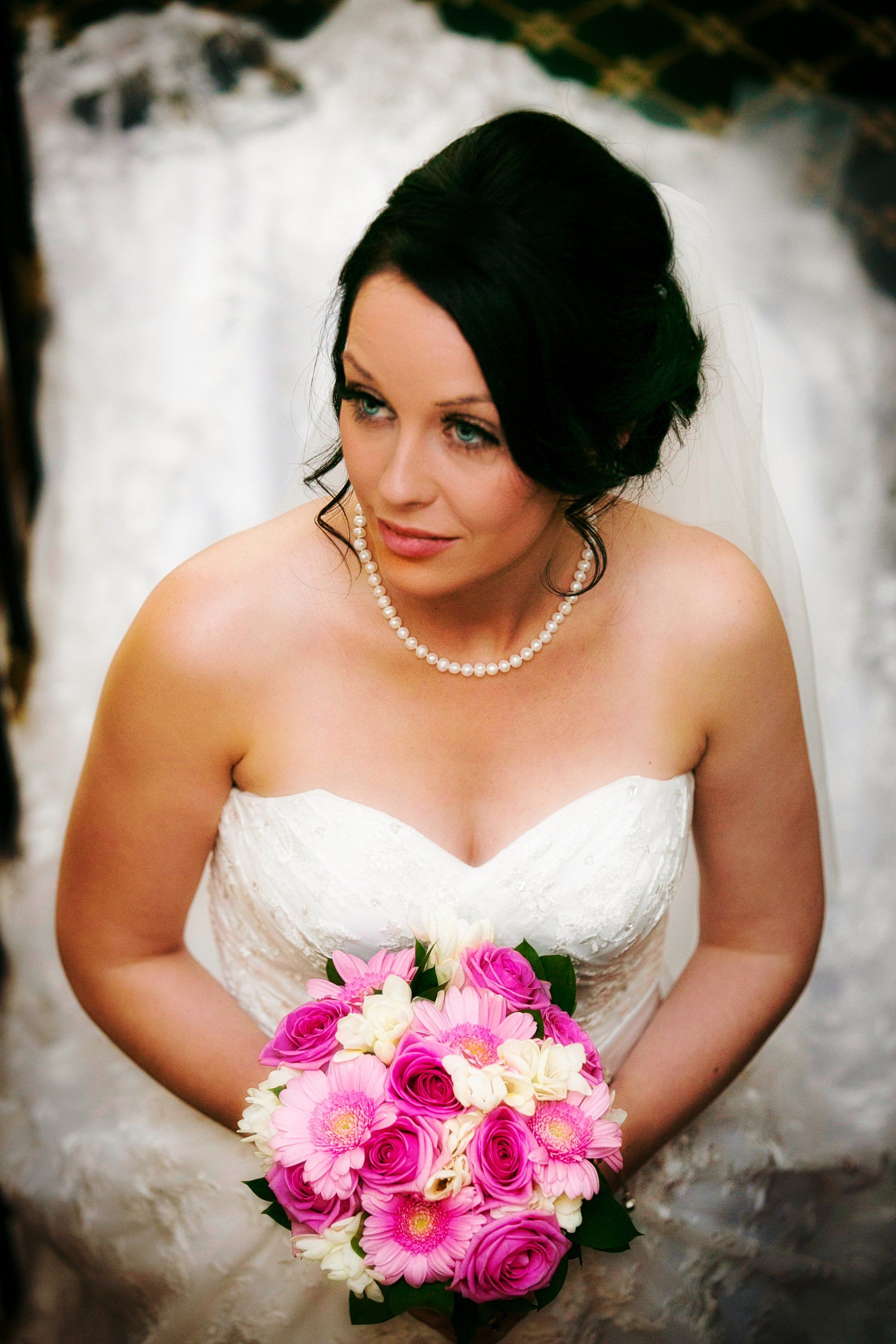 Bride in a strapless white wedding dress holding pink and white flowers, looking down.