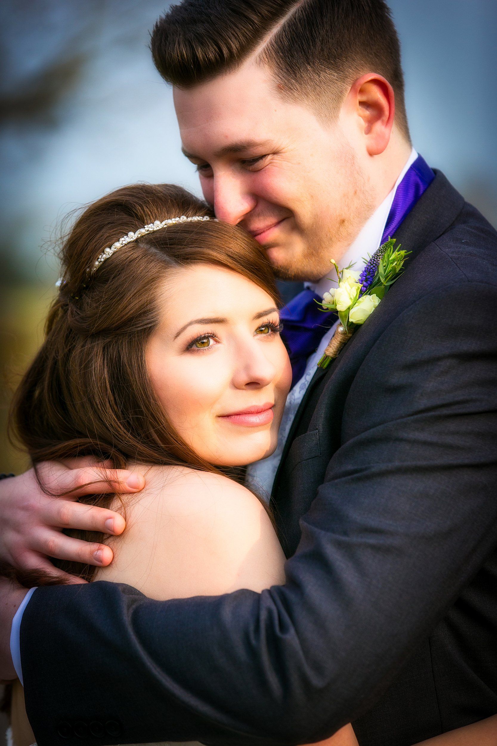 Bride and groom embracing, the man's arm around the bride. Outdoors, soft focus.