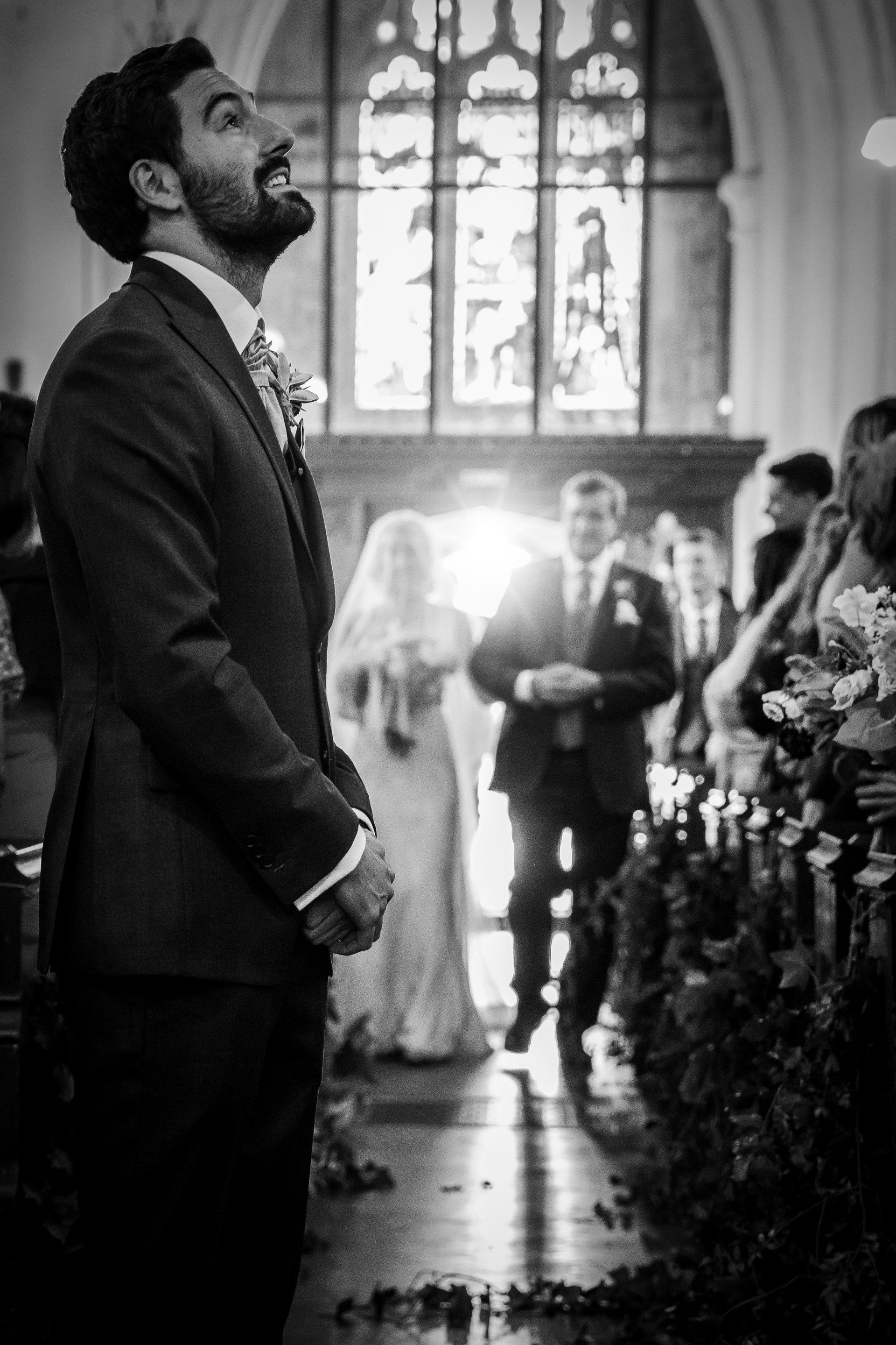 Groom smiles up as bride walks down aisle at church wedding.