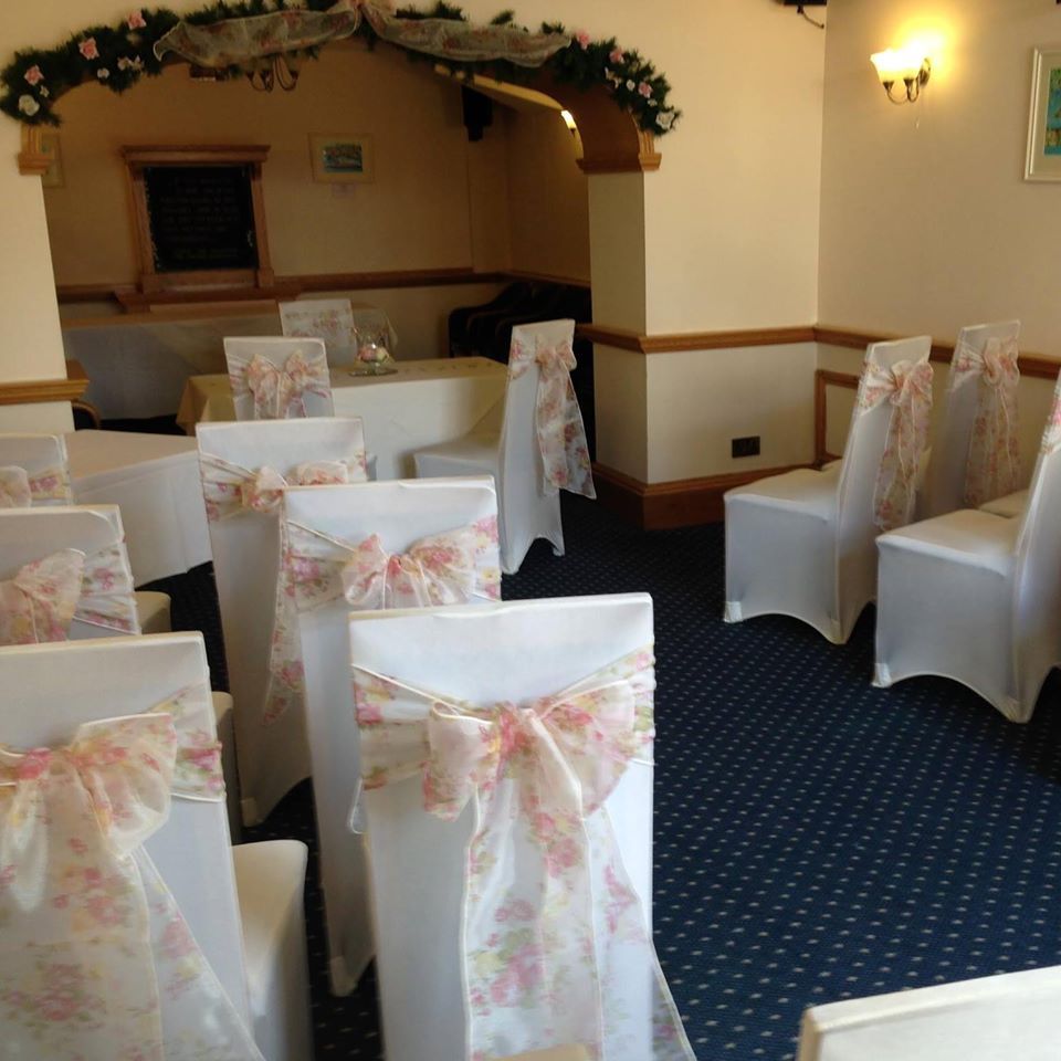 Wedding ceremony setup with white chair covers, floral bows, and archway with decorations.