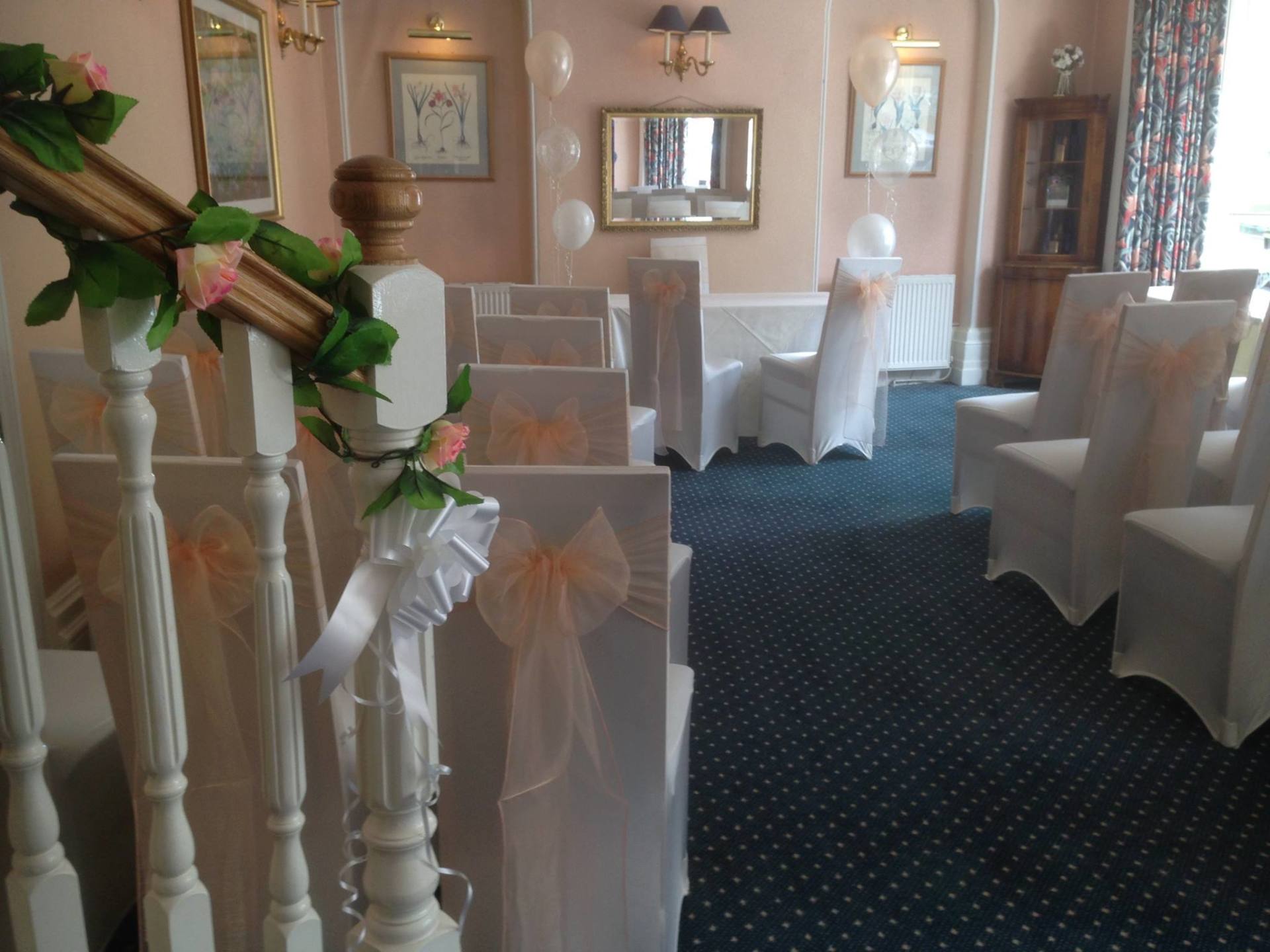 Ceremony room decorated for a wedding. White chairs with peach sashes face an adorned staircase.