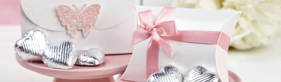 White gift boxes with pink bows and heart-shaped candies on a pink cake stand.