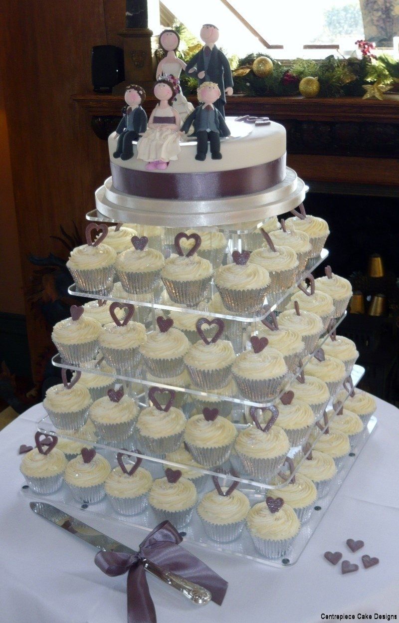 Wedding cake with cupcakes on tiers, topped with cake, figurines, and purple heart decorations.