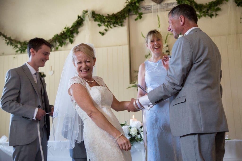 Wedding ceremony: Bride and groom smile, holding hands. Attendants and decorations visible.