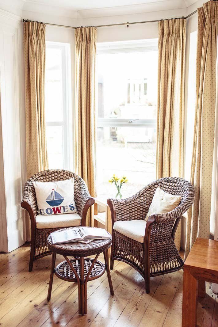 Two wicker chairs with cushions, a small table, and a window with curtains in a bright room.