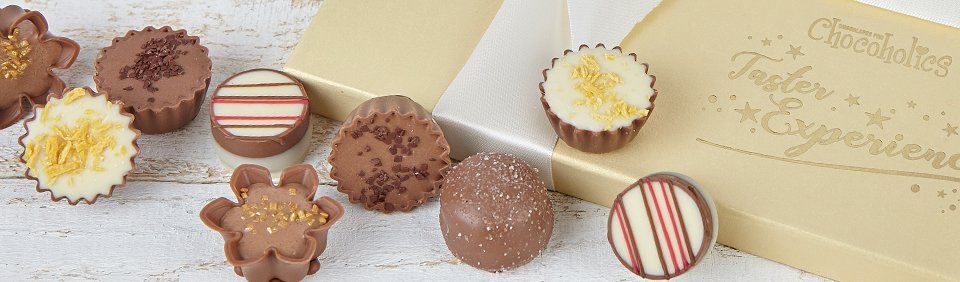 Chocolates with various toppings next to a light-colored box. Some chocolates have stripes or flower shapes.