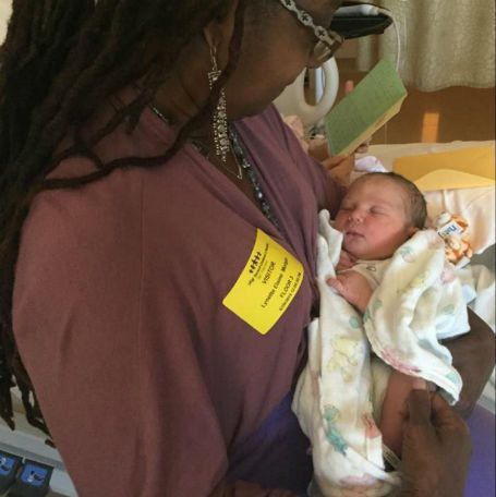 Woman in purple holds newborn baby in hospital room.