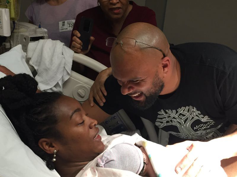 Woman giving birth in a hospital bed, smiling man leans over her, other people in background.