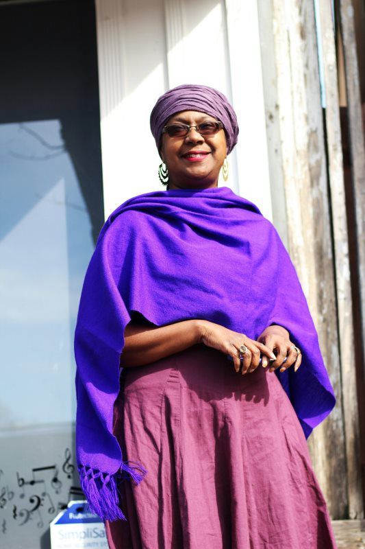 Woman in purple shawl and head covering smiles outdoors.