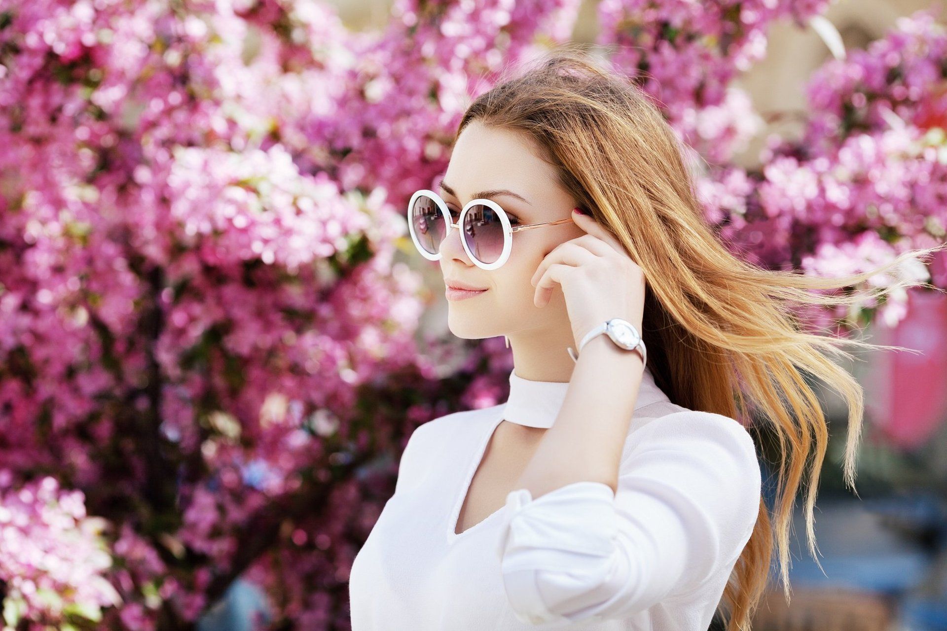 A woman wearing sunglasses is standing in front of a cherry blossom tree.