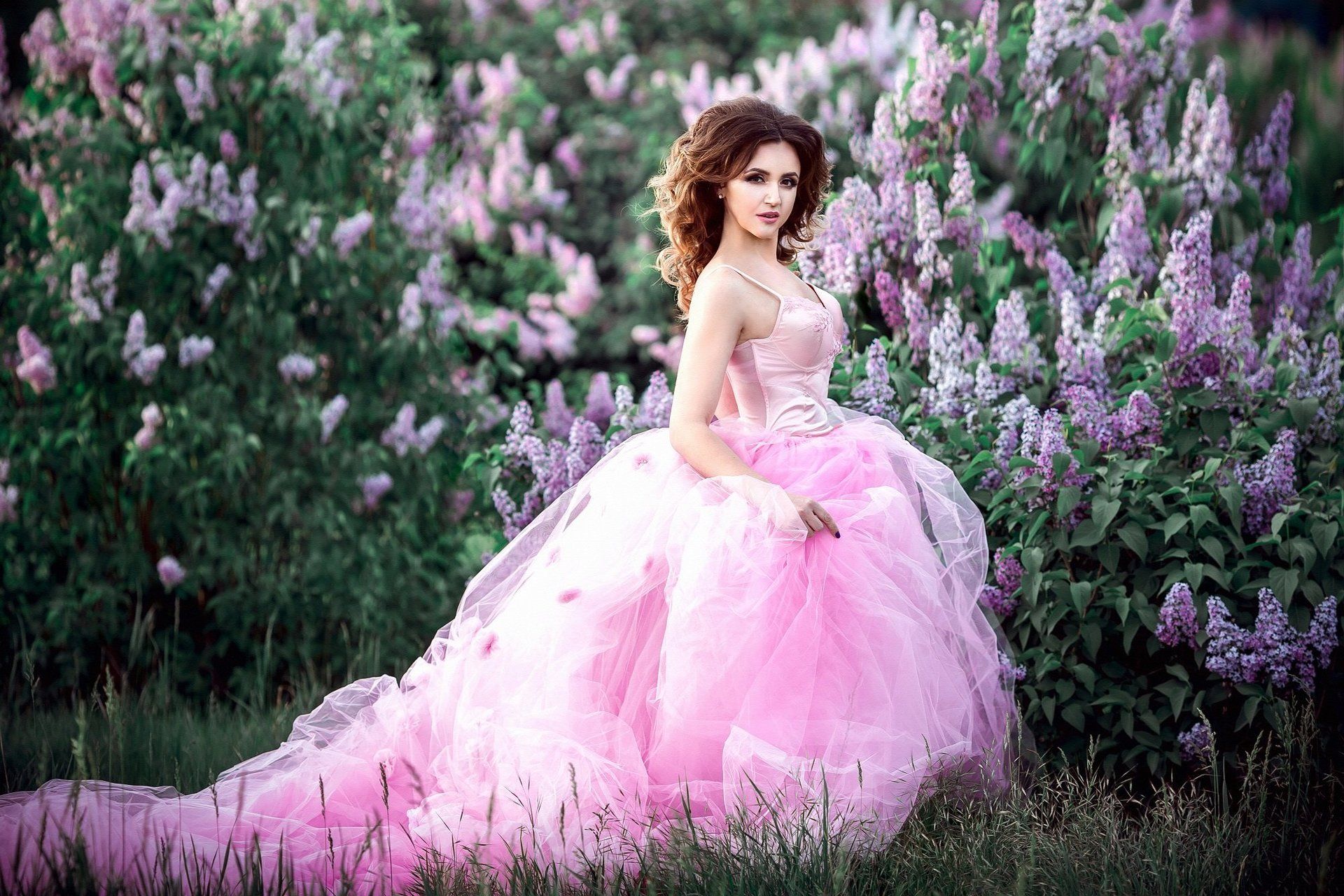 A woman in a pink dress is standing in a field of purple flowers.