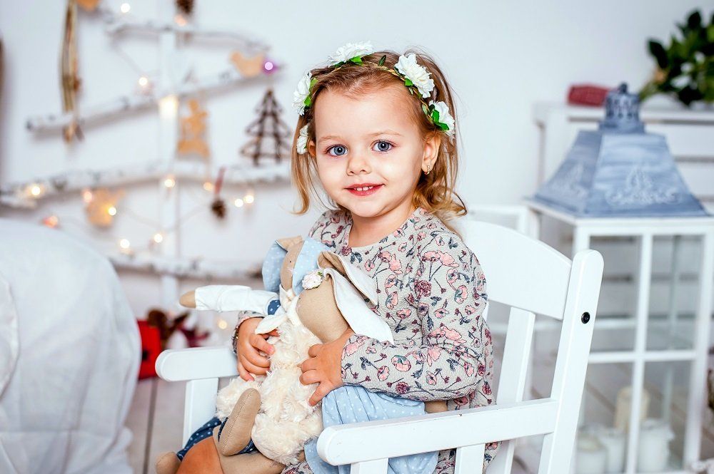 A little girl is sitting in a rocking chair holding a stuffed animal.
