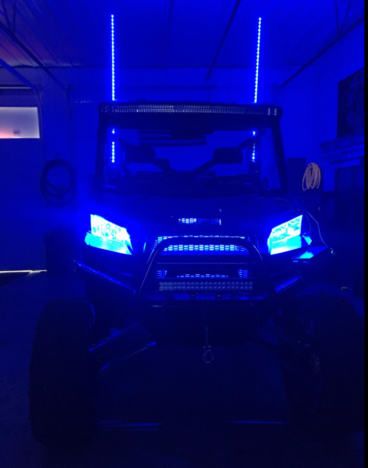 Blue-lit off-road vehicle in a garage with glowing headlights and roof lights.