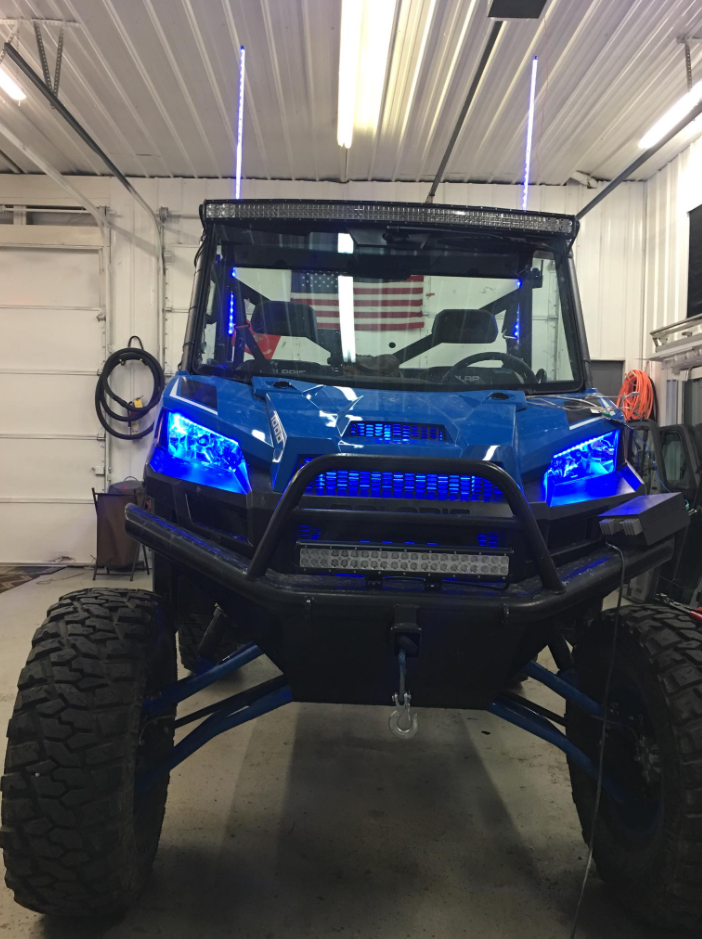 Blue off-road side-by-side utility vehicle in a garage, front view with large tires and bumper guard.