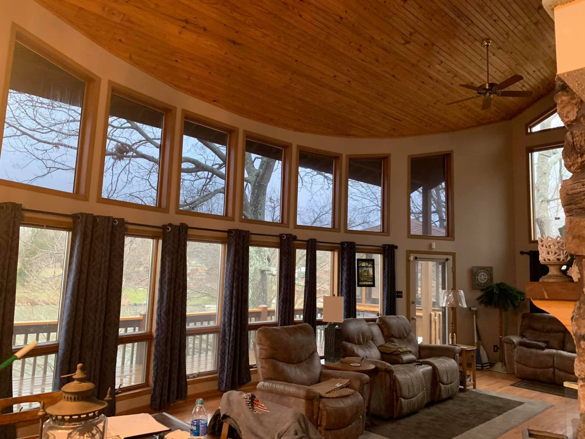 Spacious living room with tall windows, wood ceiling, leather recliners, and a stone fireplace.