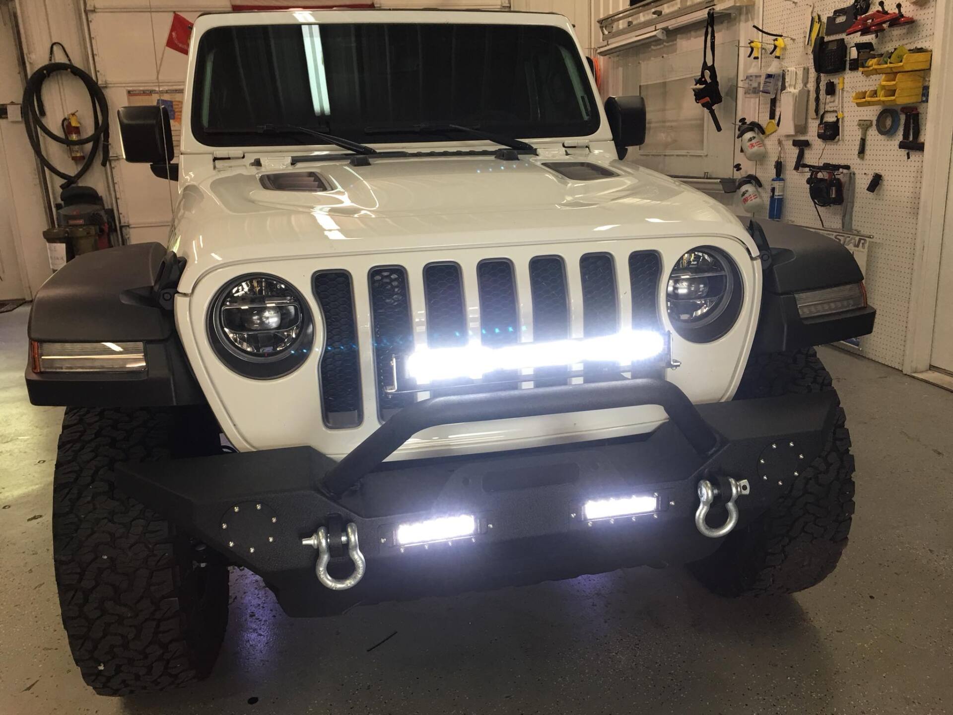 White Jeep Wrangler with bright LED lights parked in a garage.