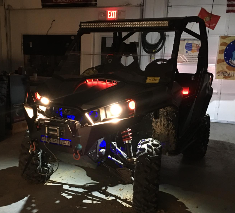 Off-road UTV with bright headlights in a dim garage, red hood glowing and large tires visible