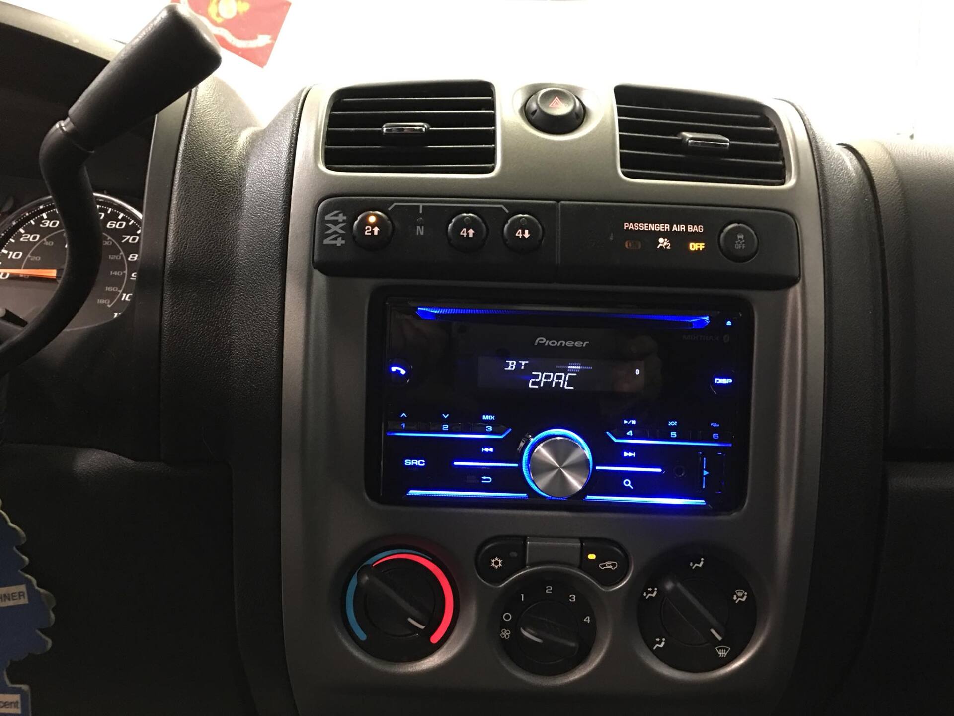 Car dashboard center console with blue-lit stereo display, vents, and climate control knobs.