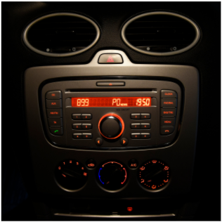 Car dashboard center console with illuminated radio and climate controls in a dark interior