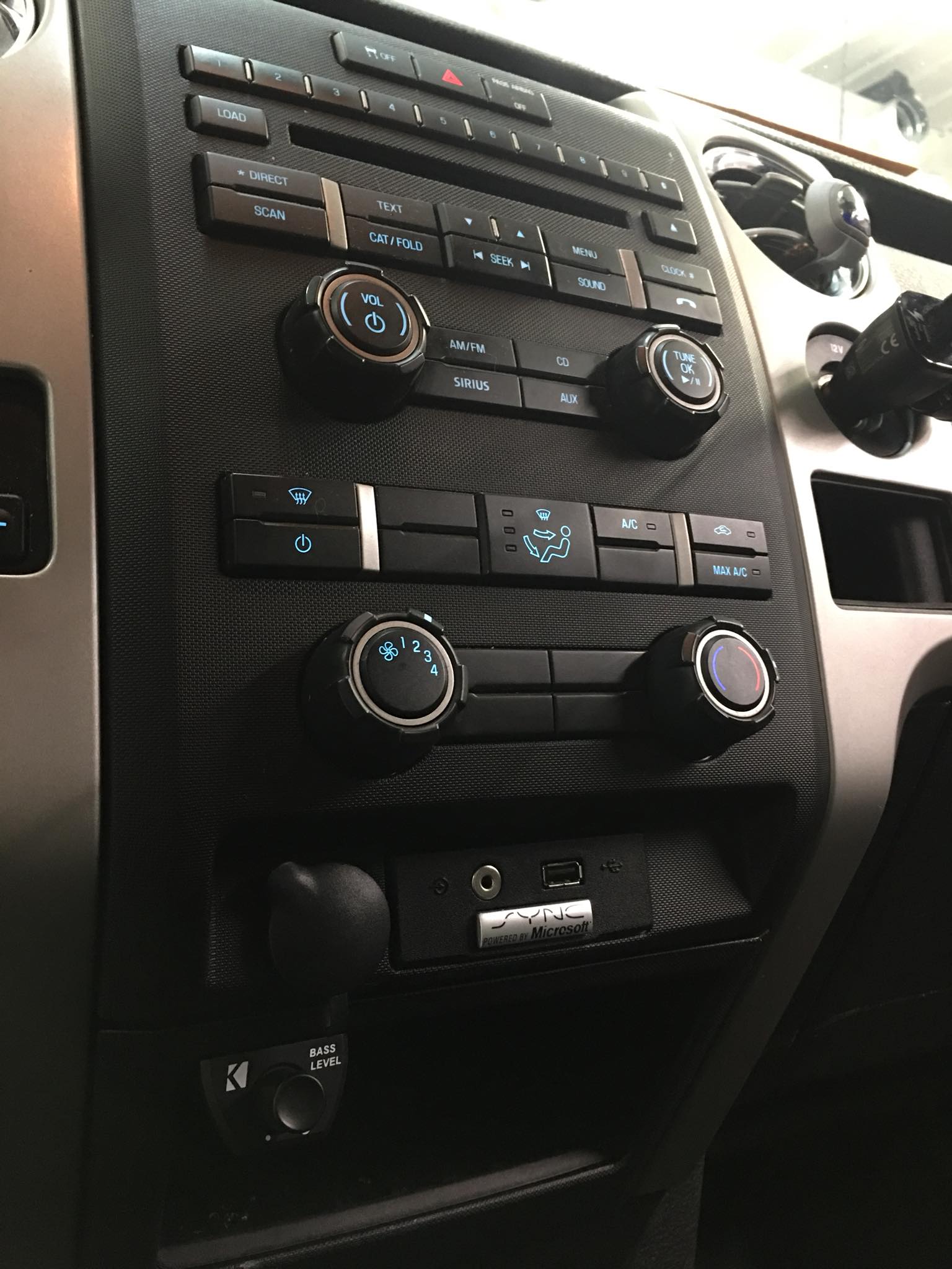 Car dashboard center console with air vents, radio, and climate control knobs on a carbon-fiber panel