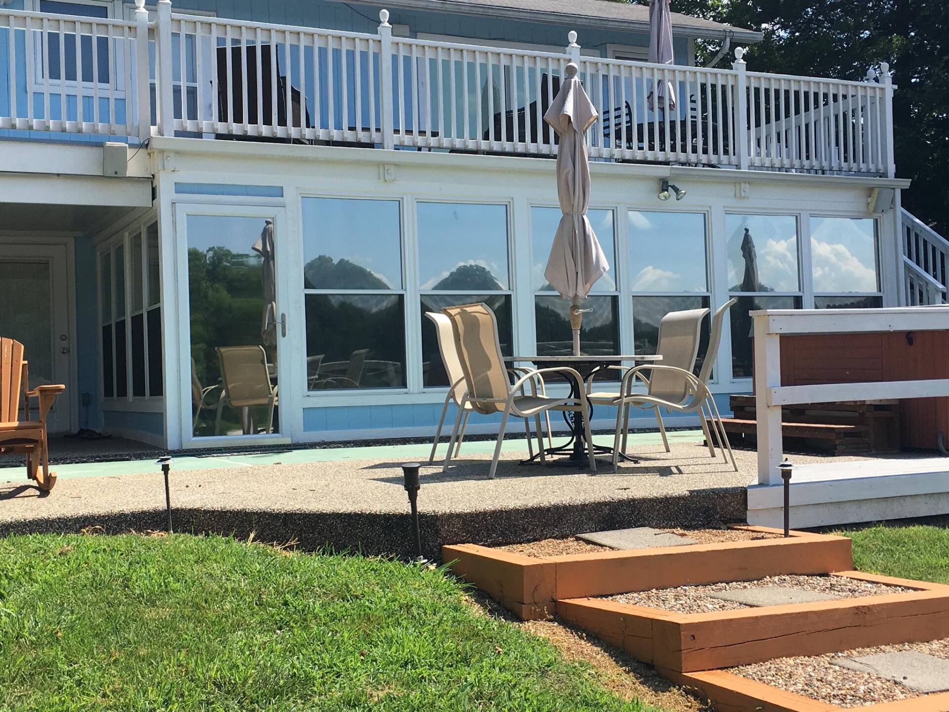 Patio with glass doors, outdoor chairs and table, umbrella, and wooden steps beside a deck over a grassy yard