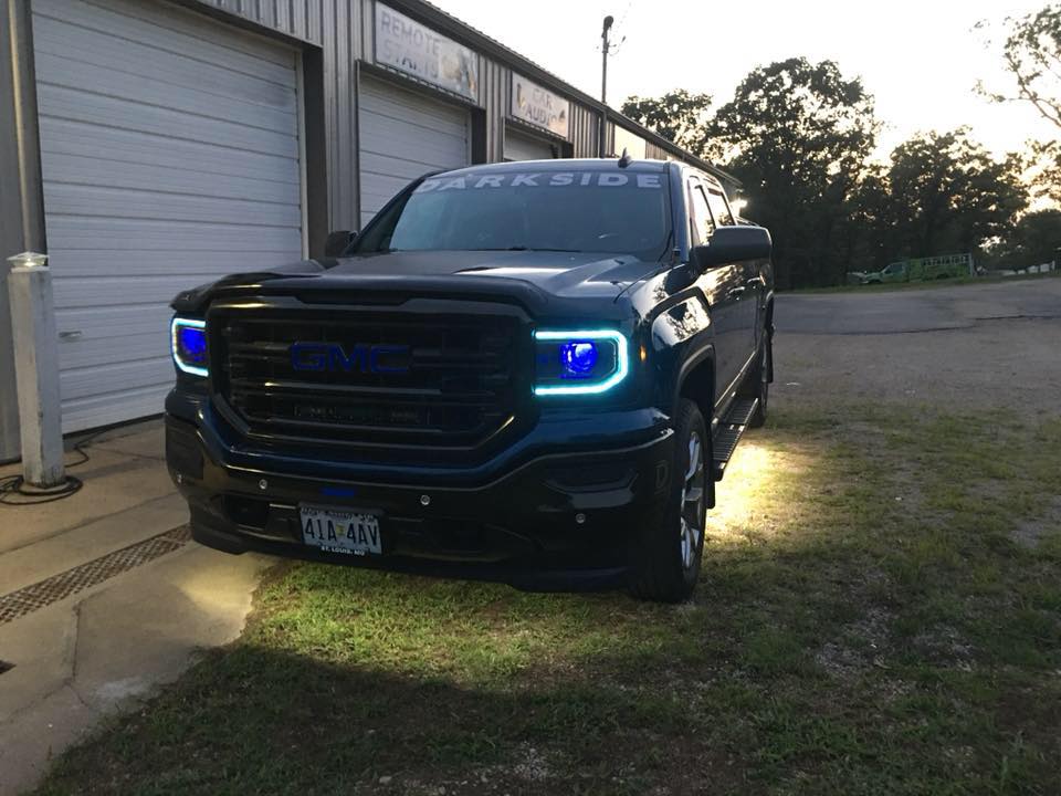 Black pickup truck with blue headlights parked beside a building at dusk