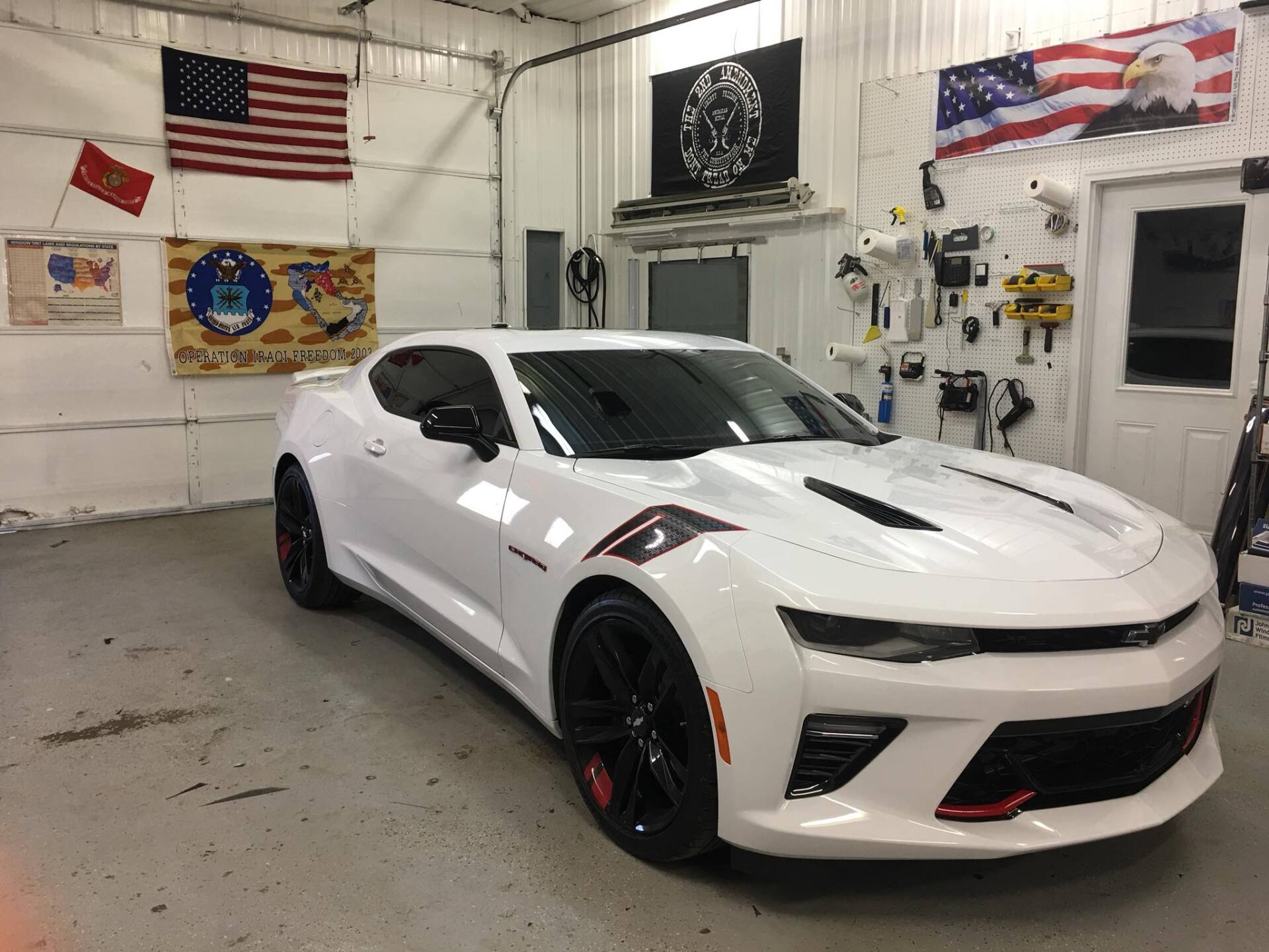 White sports car in a garage workshop with flags and tools on the walls