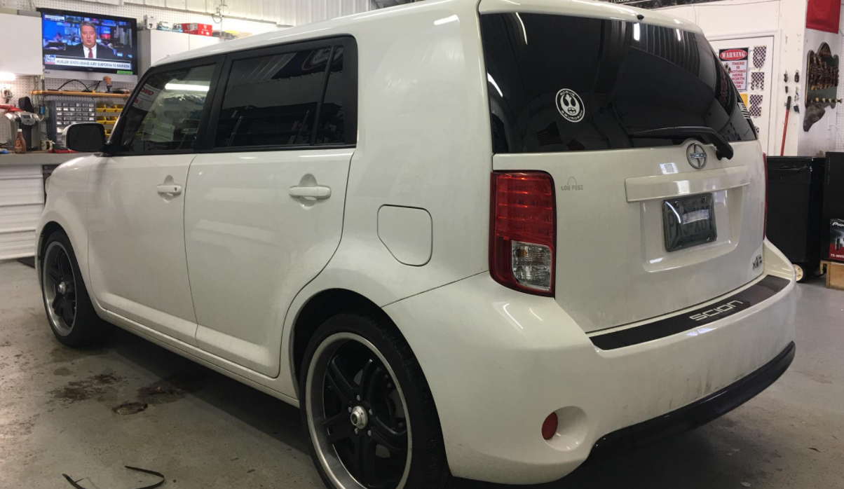 White Scion xB parked indoors at an auto shop, rear three-quarter view.