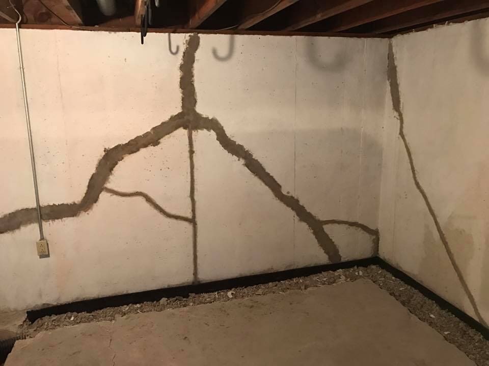 Cracked basement wall with a dark, patched network across the white surface.