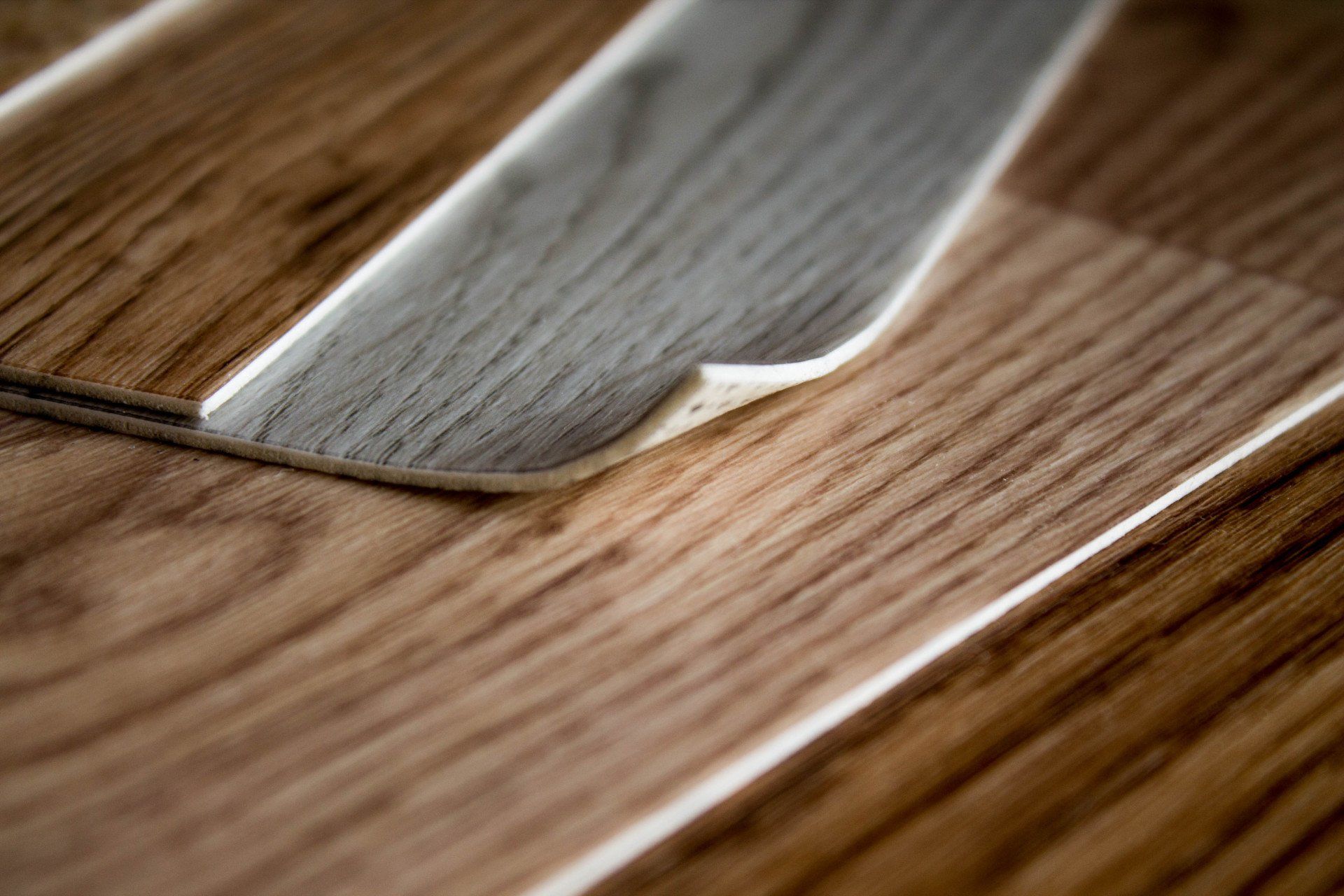 Close-up of wood-look flooring with a piece partially peeled up, revealing a lighter layer.
