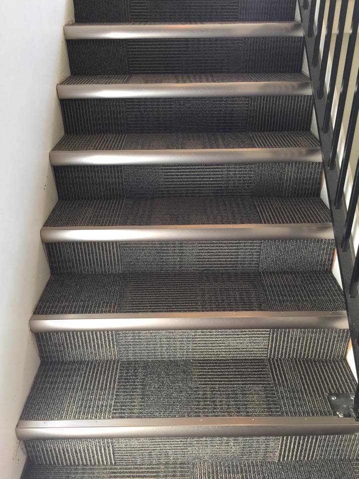 Carpeted staircase with metal edging, dark gray and black pattern.