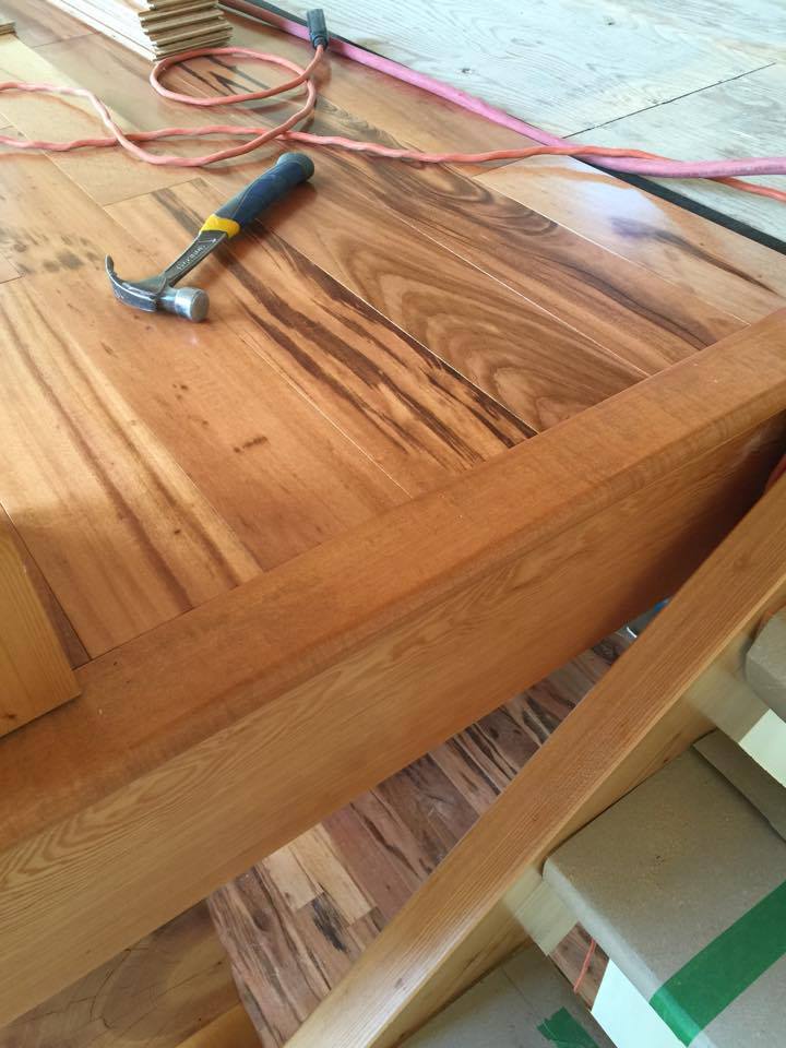 Hammer and wood flooring in progress, with wood planks, electrical cord, and a wooden stair.