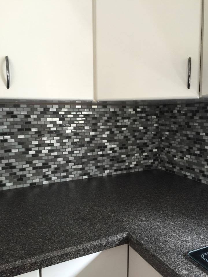 Kitchen with dark countertop, mosaic backsplash in gray and white tones, white cabinets.