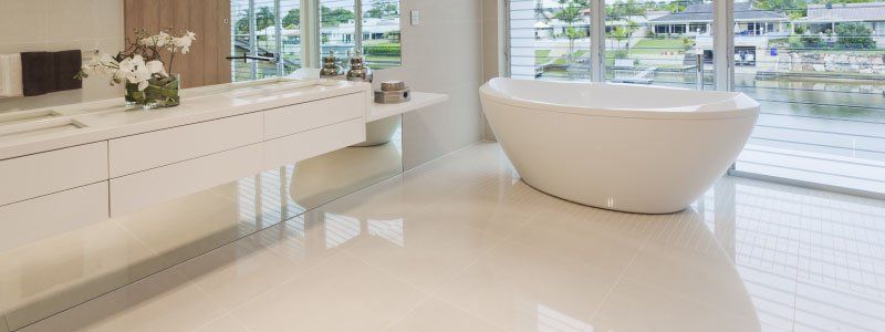 Modern bathroom with white flooring, a freestanding bathtub, and a large window overlooking a body of water.