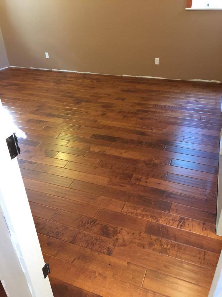 Hardwood floor in a room with tan walls. The floor is brown and glossy with a partially open white door.