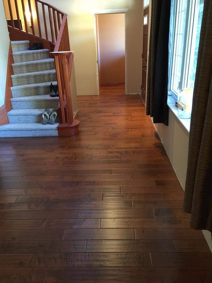 Hardwood floor leads to a stairwell, doorway and window with brown curtains.