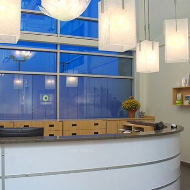 Espace de réception avec un bureau blanc incurvé, des armoires en bois et des lumières suspendues décoratives près d'une fenêtre avec une teinte bleue.