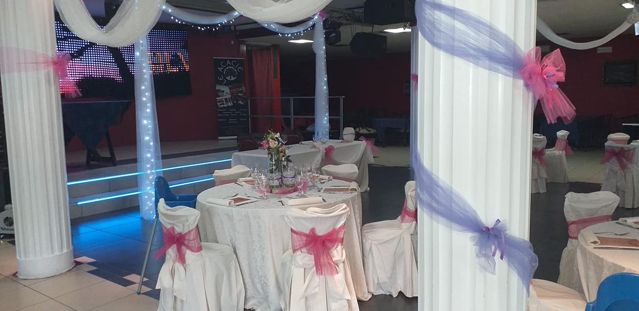 Tavoli da banchetto decorati con coprisedie bianchi e fiocchi rosa in una sala eventi scarsamente illuminata