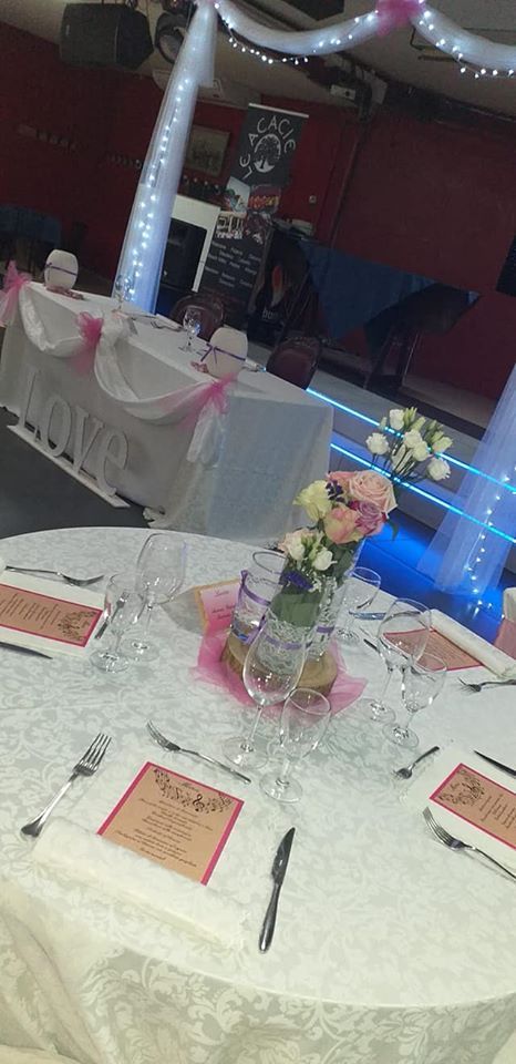 Tavolo da banchetto decorato con centrotavola floreali e sedie bianche in una sala eventi illuminata di rosso.