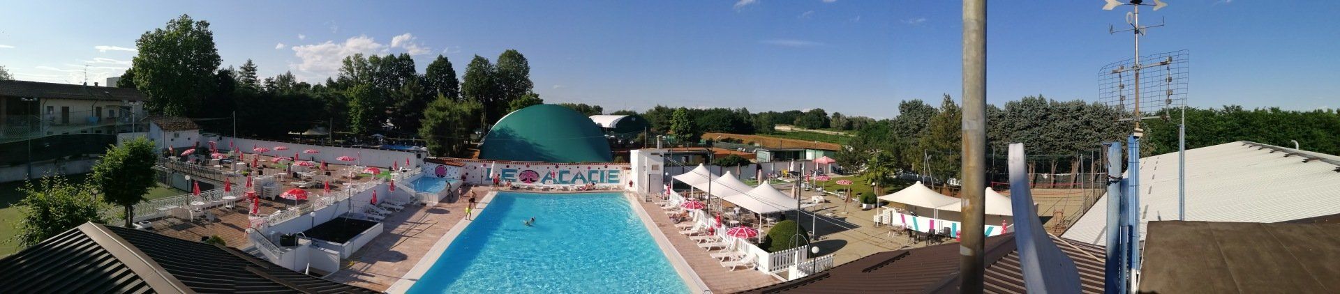 Piscina all'aperto del resort con acqua cristallina, lettini, ombrelloni e palme sotto un cielo limpido.