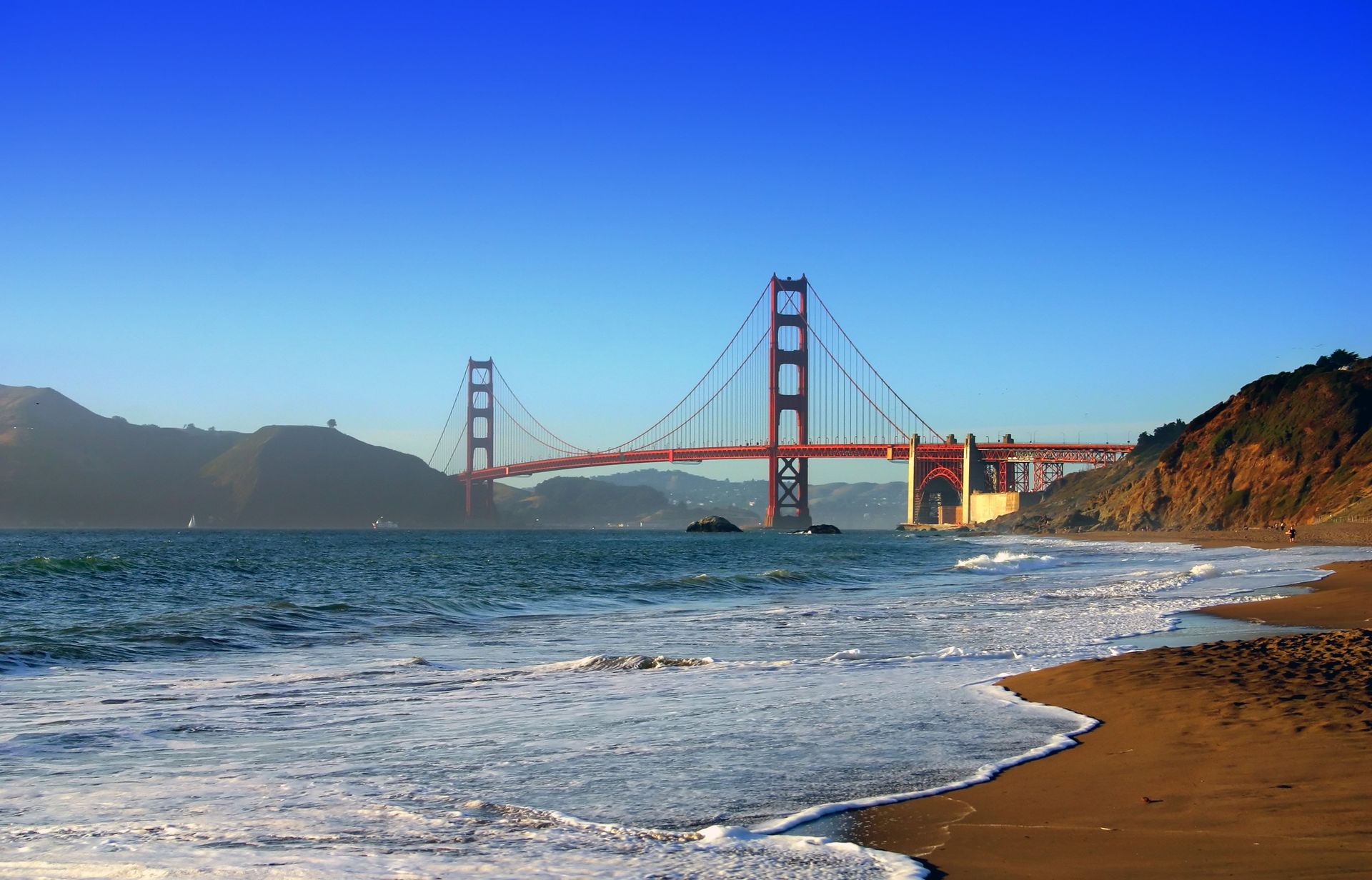 Golden Gate Bridge over a sandy beach with waves and a clear blue sky
