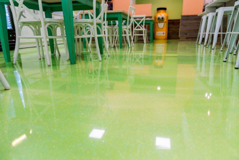 Green glossy floor in a café or classroom with white chairs and tables reflected above it