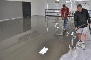 Two people smoothing wet gray concrete inside a large empty room