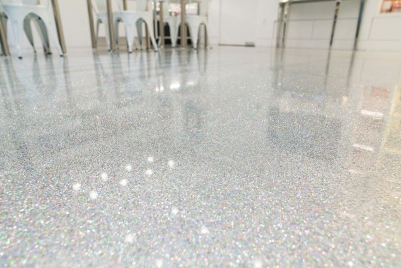 Bright speckled white floor in a modern room with stools and reflections in the background